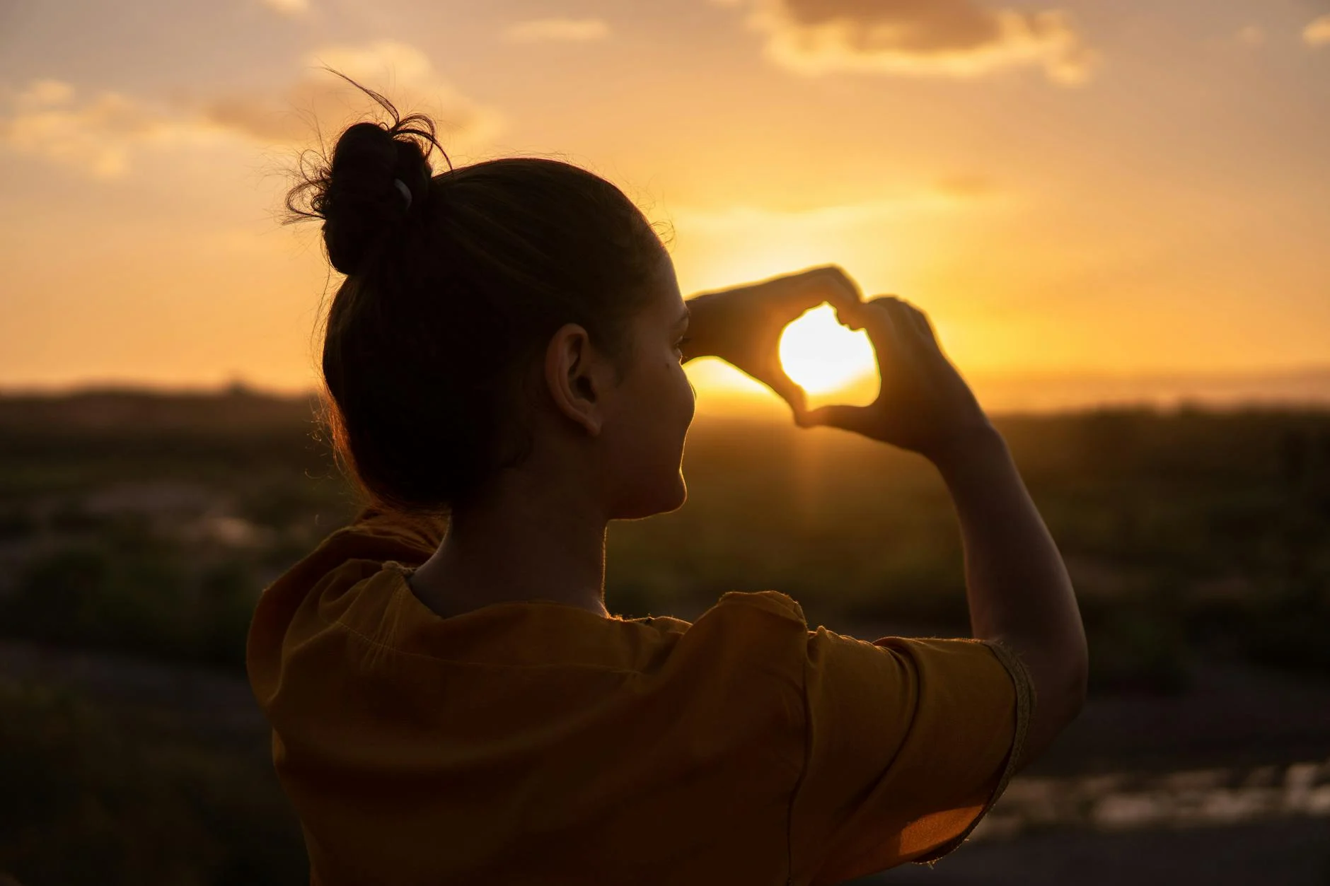 woman showing hearth shape with her hands, sunset background